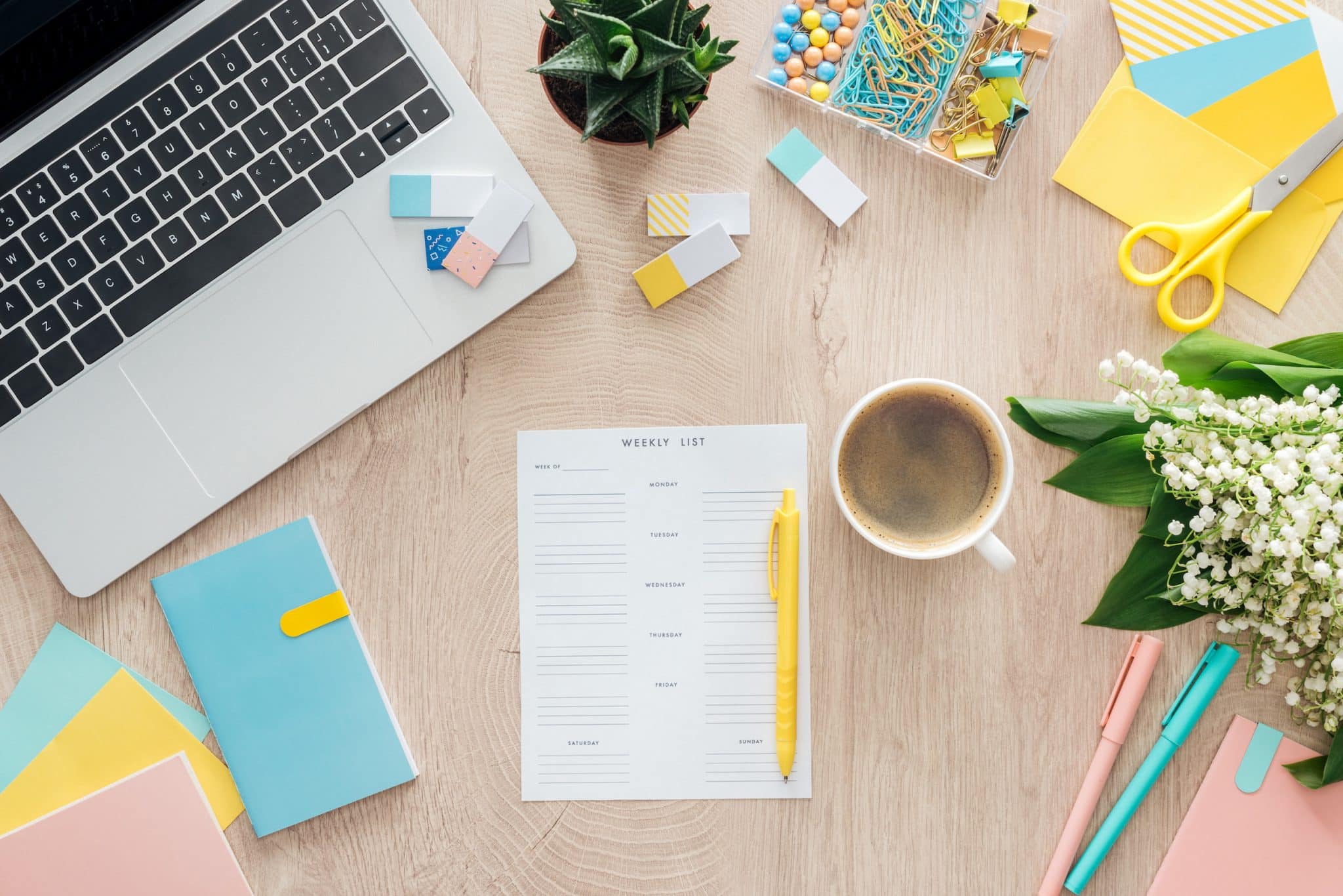 top view of weekly list, cup of coffee, stationery, laptop and flowers on wooden table