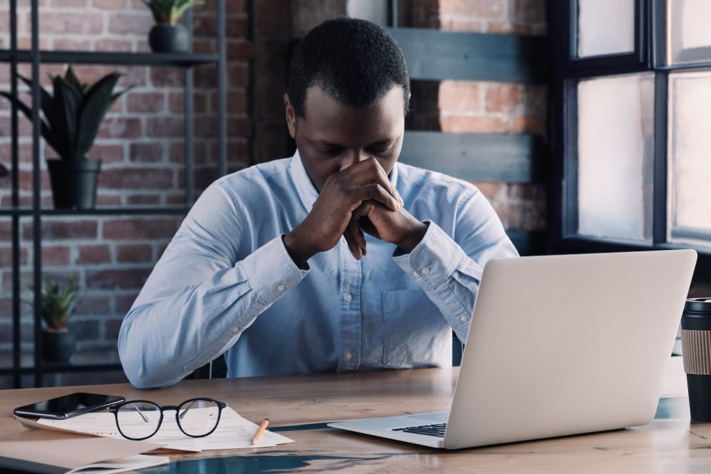 Tired and frustrated african business man at workplace in office holding his head on hands