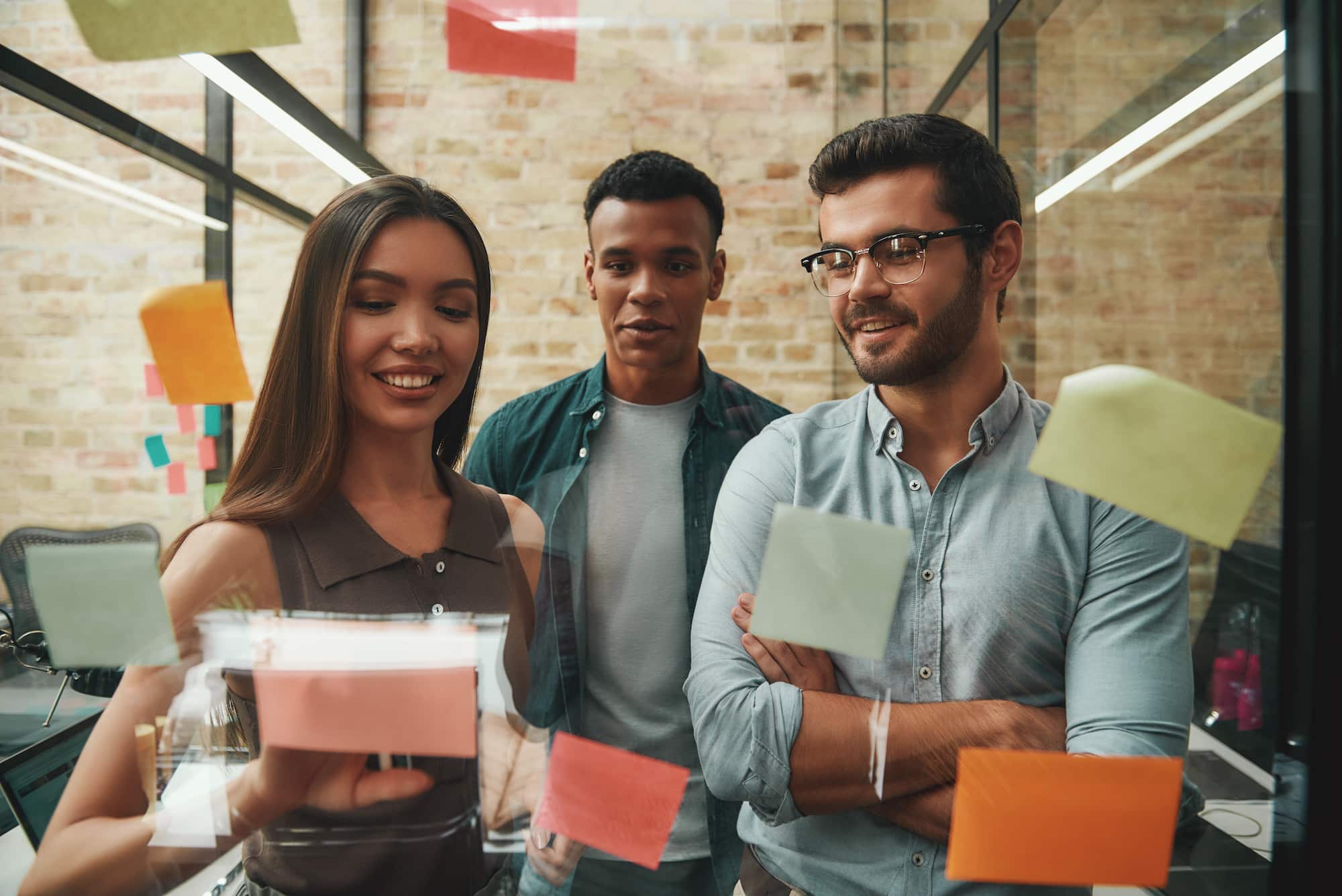 Fresh ideas. Cheerful male and female colleagues planning working process and using colorful stickers while standing in front of glass wall. Teamwork. Project management