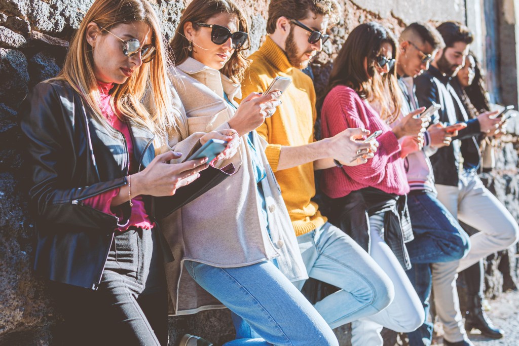 
Millennial generation people using smartphones. Young people addicted from social network application dependency concept. Friends using cell phones against an ancient wall. Mid section