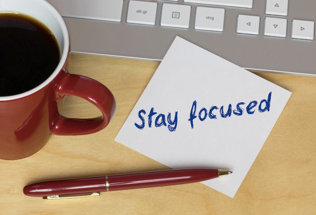 Desktop with coffee cup, pen and post-it note with stay focused written