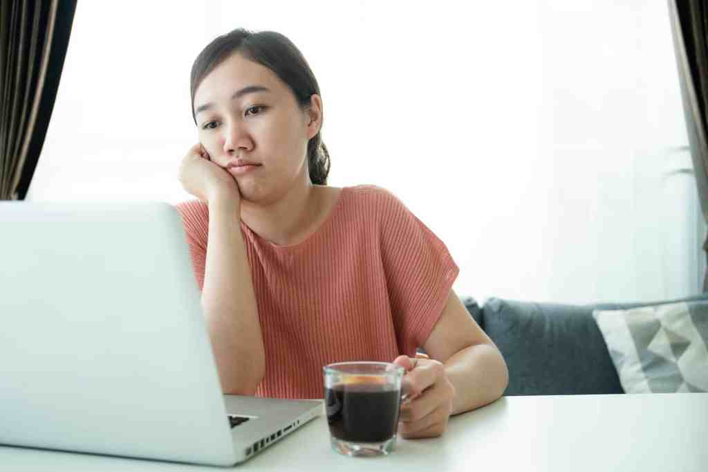 Young Asian woman bored in online meeting and work from home, woman tired in her work and online meeting. Unmotivated freelance worker - bored Asian girl working at home in morning.