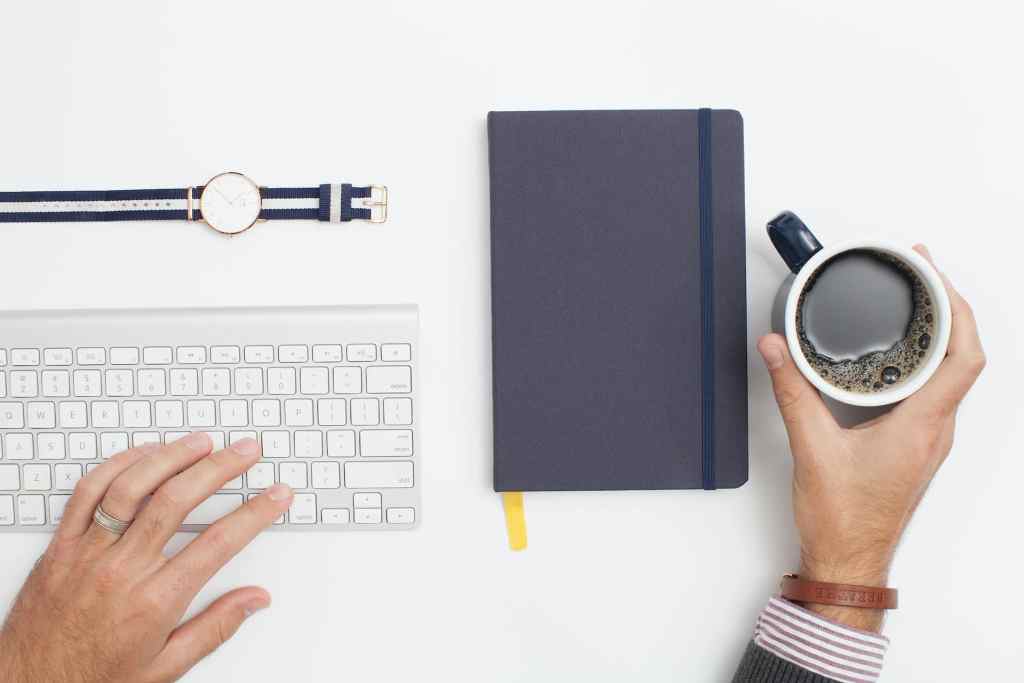 minimalist simple desk with keyboard, watch, notebook and coffee mug.