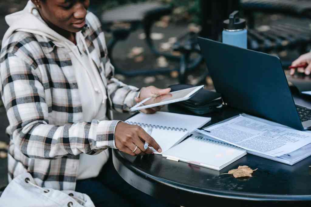 Black female student studying outside in fall with notebook and laptop