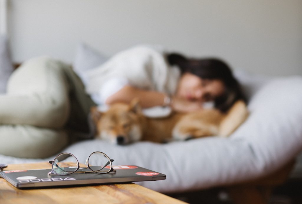 woman enjoying a nap beside her shibe inu dog while laptop lays to the side closed