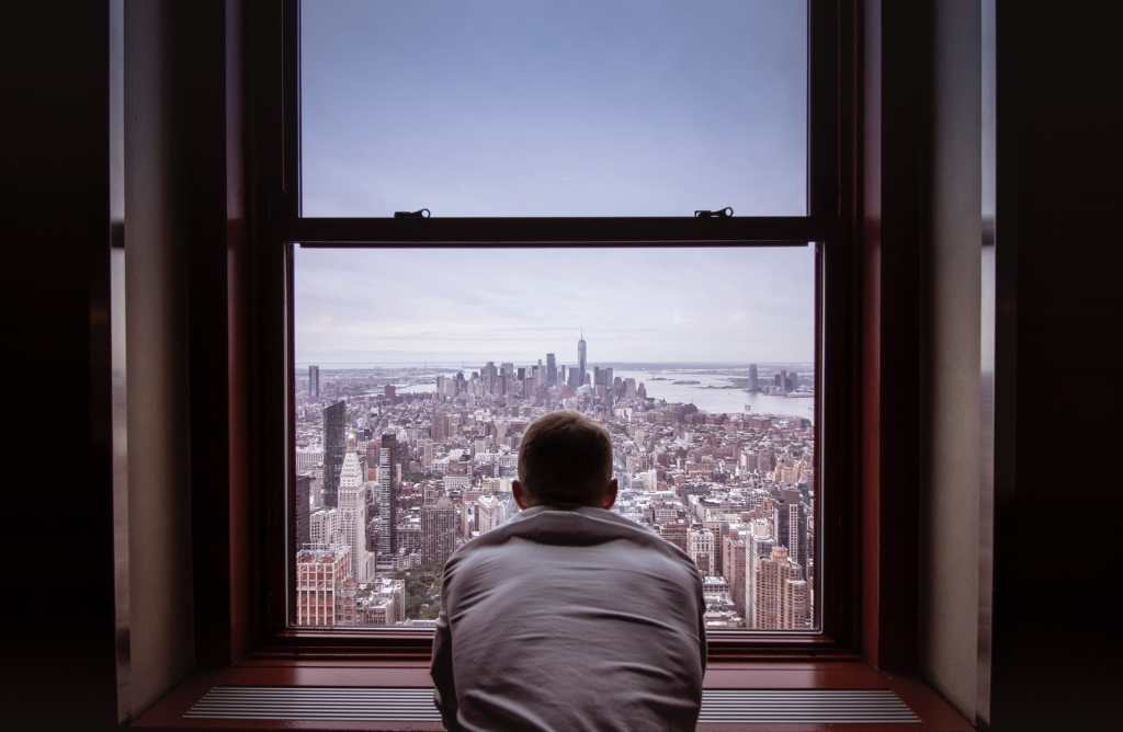 Man looking out window at city surveillance big tech fomo