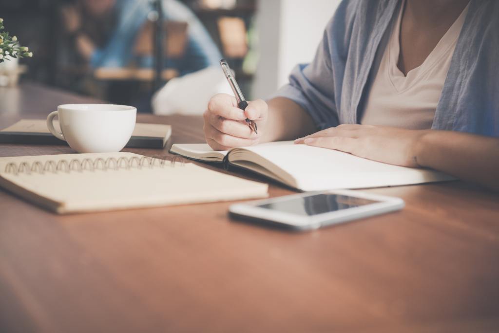 writer working at desk with notepad and smartphone