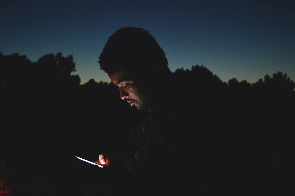 Black man doomscrolling smartphone outdoors at night